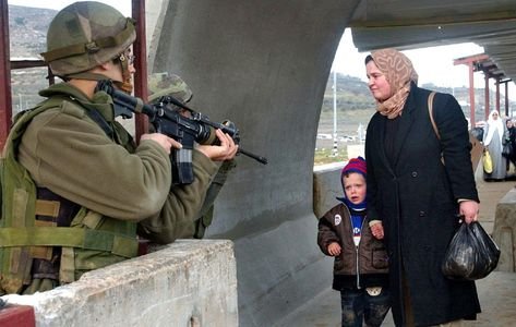 Photo of a Palestinian mother and her children as they pass in front of Israeli soldiers aiming their weapons..