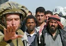 An Israeli soldier signals for people to stop. Numerous Palestinians wait behind him.