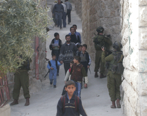 Palestinian children pass by Israeli soldiers toting machine guns.